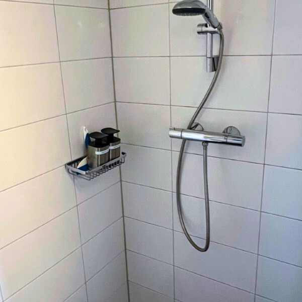 Inloopdouche met witte wandtegels, regendouchekop en verzorgingsproducten