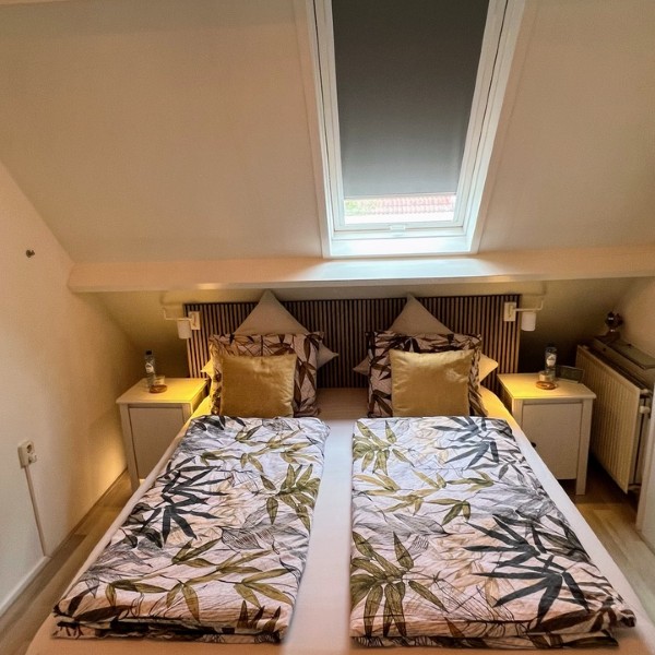 Slaapkamer met tweepersoonsbed, bladmotief dekbedovertrek, dakraam en sfeerlamp