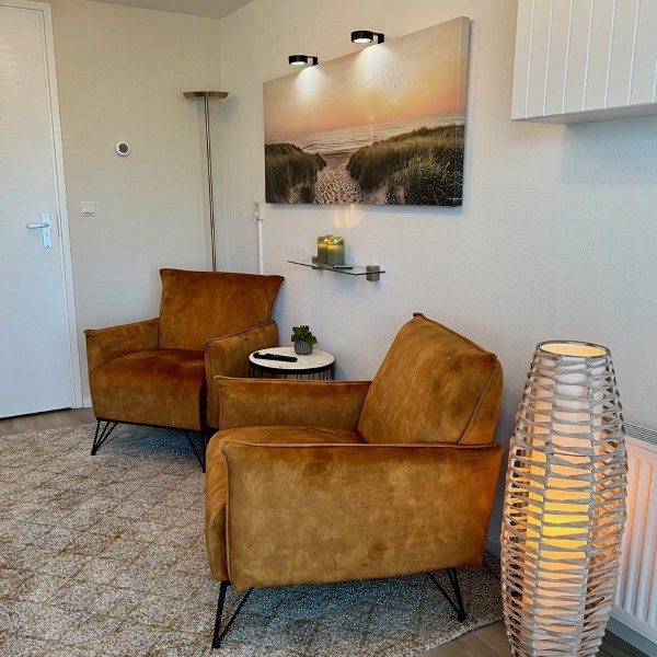 Zithoek met warme fauteuils, duinenschilderij en sfeervolle rieten vloerlamp