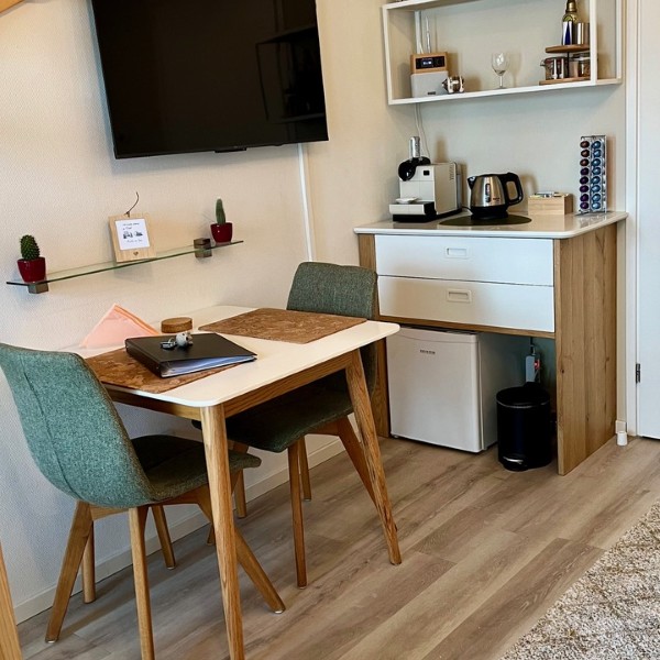 Overzicht van de woonruimte met eettafel, flatscreen TV, kitchenette en houten vlizotrap